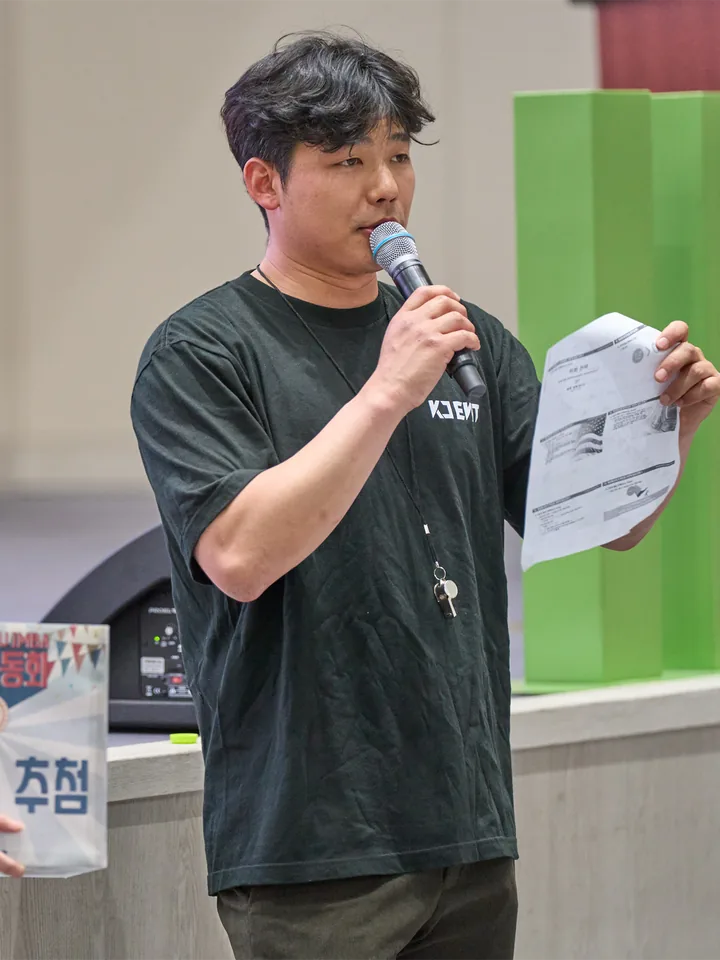 마이크와 진행 대본을 들고 행사를 이끄는 장면