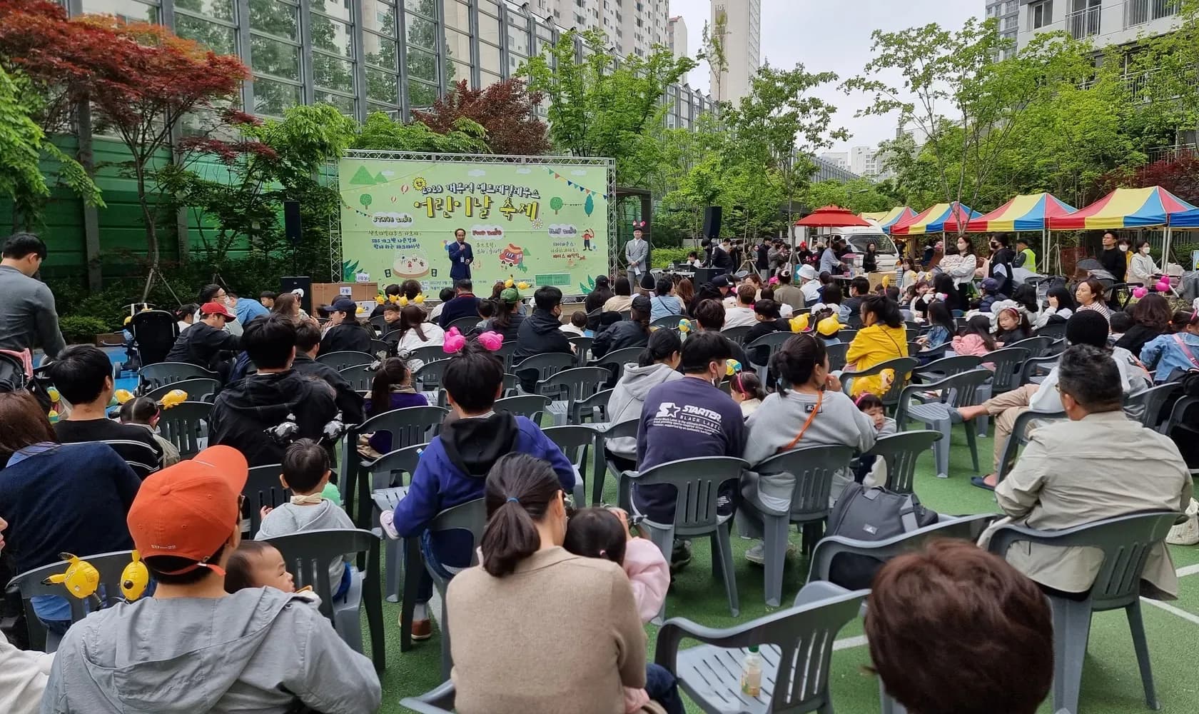 아파트 단지 광장 무대 앞에 의자를 놓고 모인 어린이날 축제 참가자들