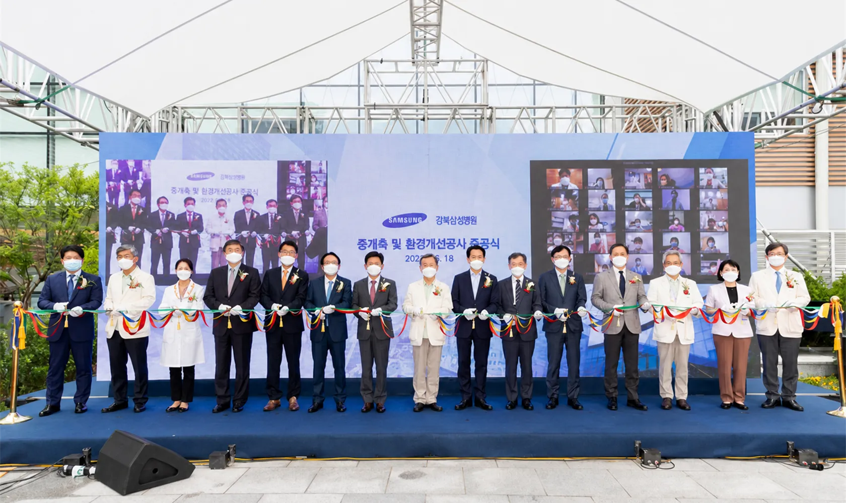 야외 준공식 무대에서 오색 테이프를 한 줄로 잡고 선 참석자들