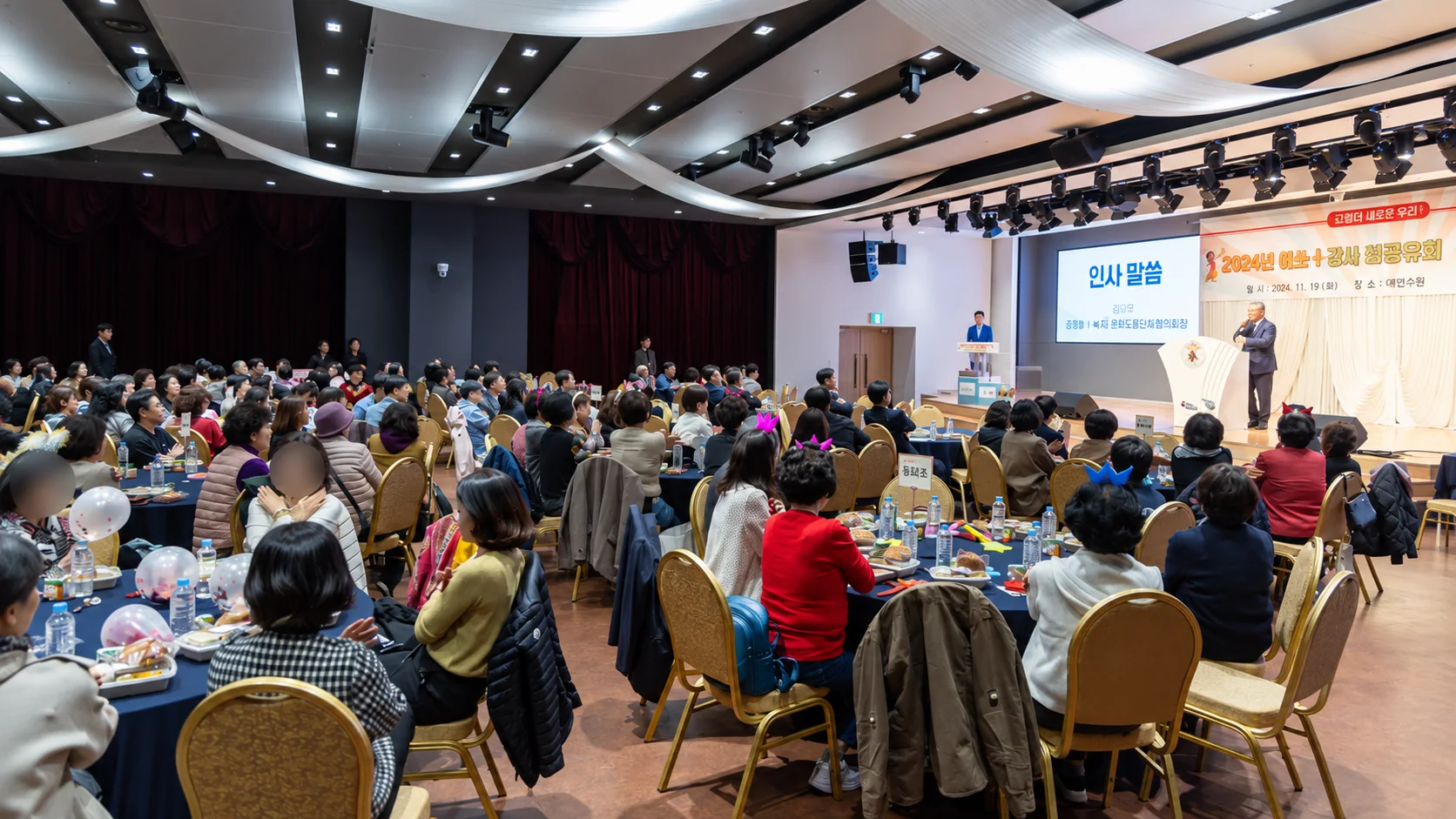연회장 원탁 객석 너머 무대 화면에 인사말씀 순서가 뜬 성과공유회 진행 모습