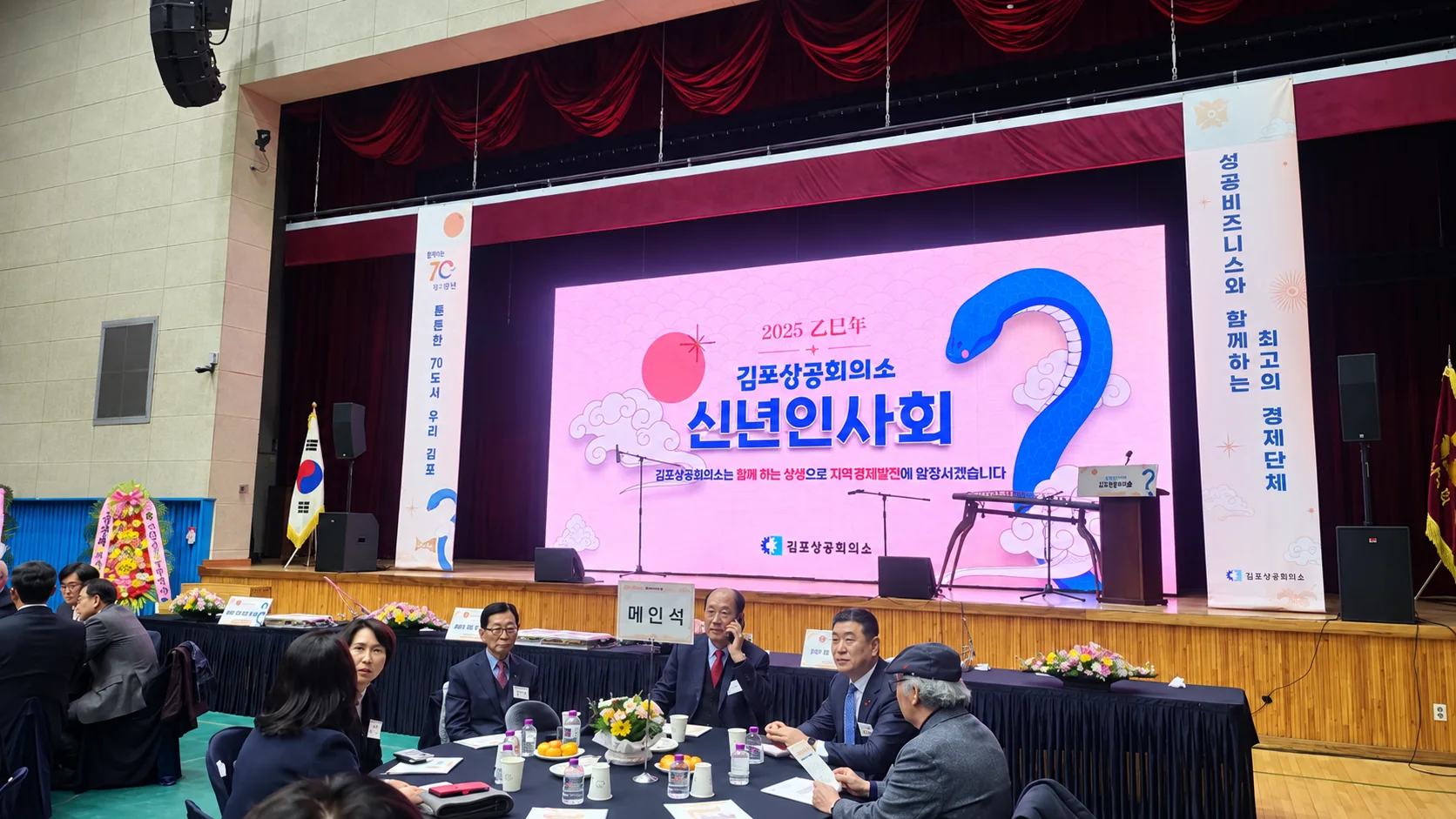 강당 무대 LED 화면에 신년인사회 타이틀이 뜨고 원탁 내빈석에 참석자들이 앉아 있는 모습