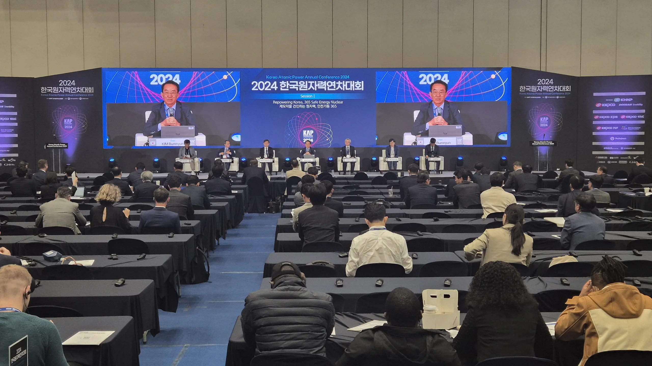 컨퍼런스 패널 토론 무대 좌우 LED 화면에 발표자 중계 화면이 송출되는 객석 뒤쪽 시점