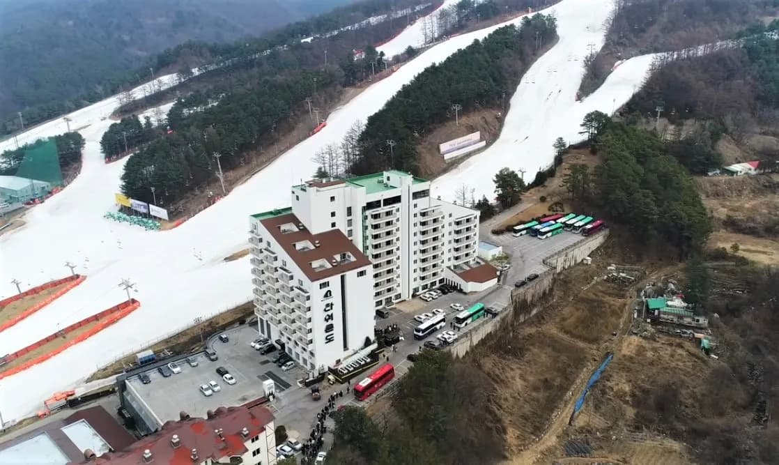 스키 슬로프 아래 리조트 건물 앞에 줄지어 선 전세버스와 주차장